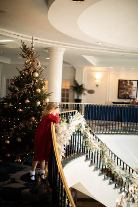 Little girl next to Christmas tree by the grand staircase